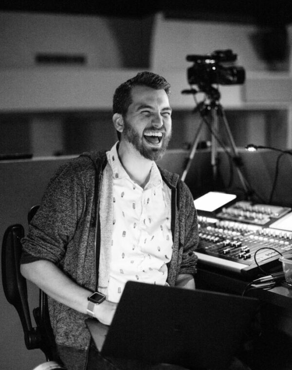 Portrait of Zach Weyland at a church sound board, smiling while adjusting audio controls.